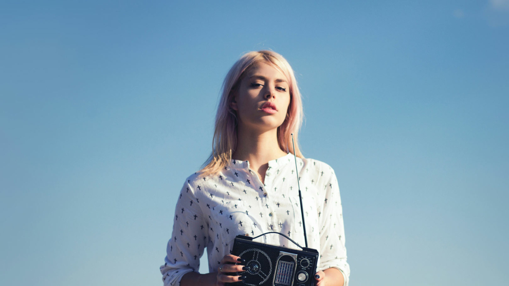 Junge blonde Frau mit Kofferradio unter blauem Himmel