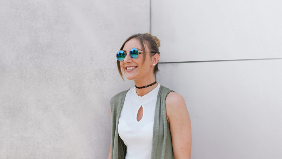 Junge Frau mit verspiegelter, runder Sonnenbrille vor einer hellen Wand